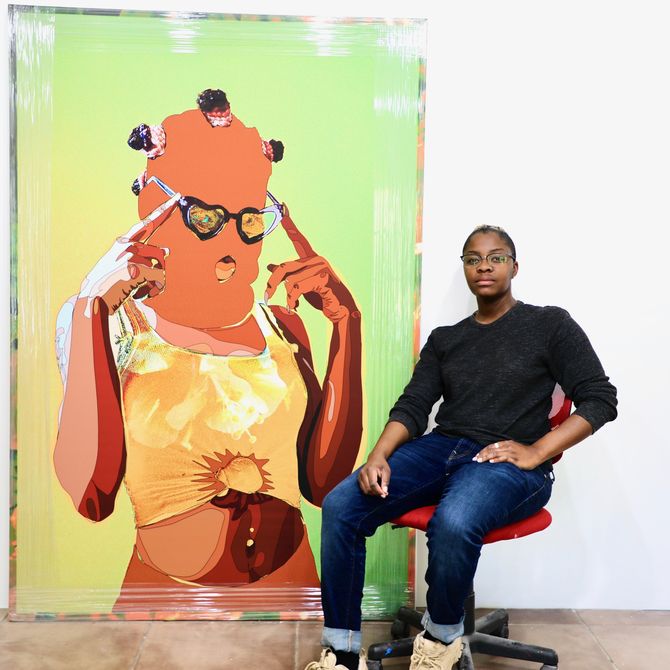 Amani Lewis sat in their studio on a red chair with a large painting behind them