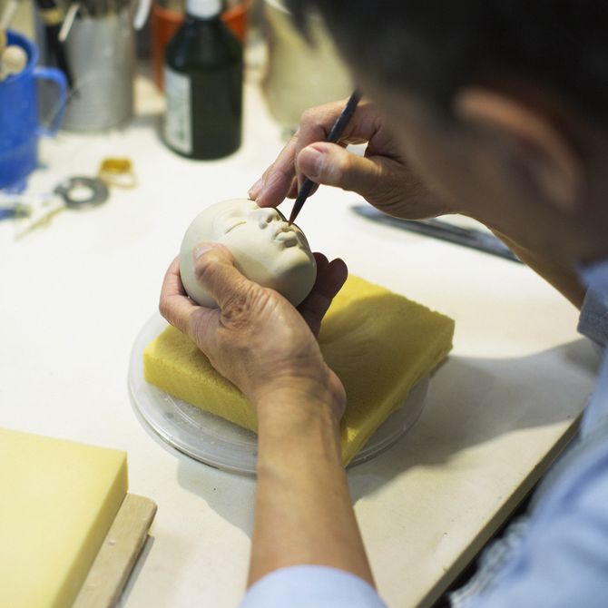 artist working into a small three-dimensional head that rests in his left-hand