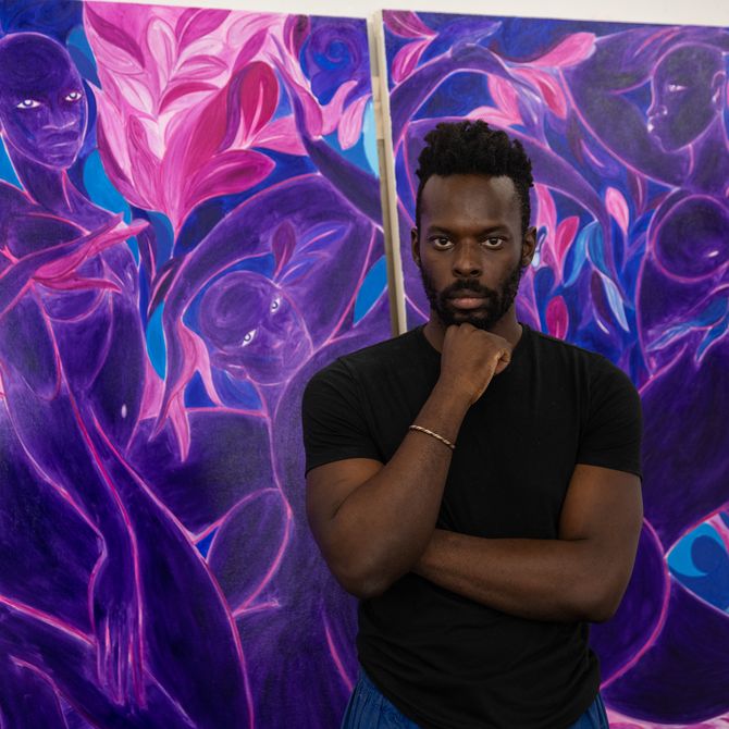 Tunji Adeniyi Jones stood in front of two large purple canvases with his head resting on his fist 