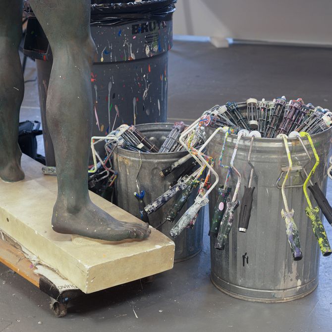 The feet of a figurative sculpture and two pots with paint rollers in them