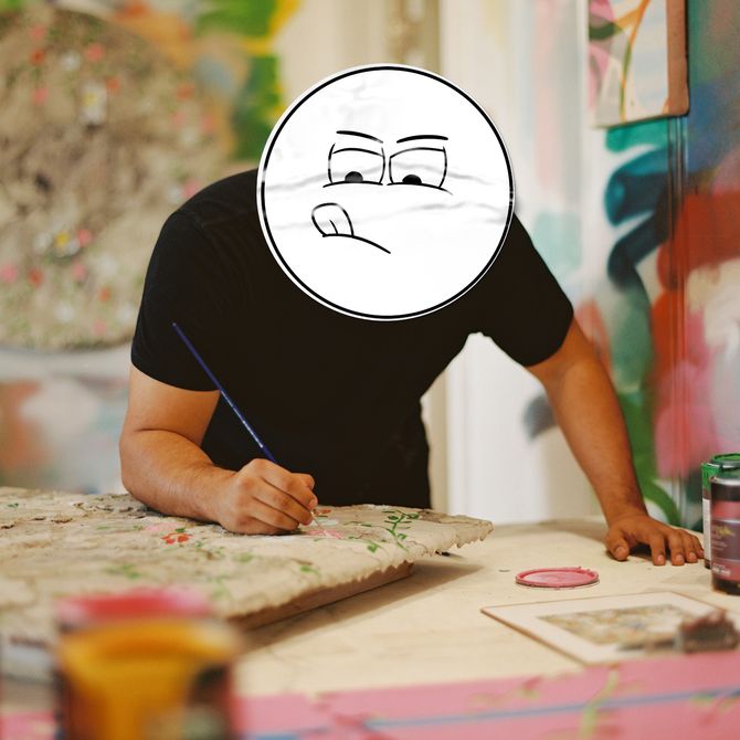 Artist Kai leaning forwards over a table with a cartoon stuck on his face 
