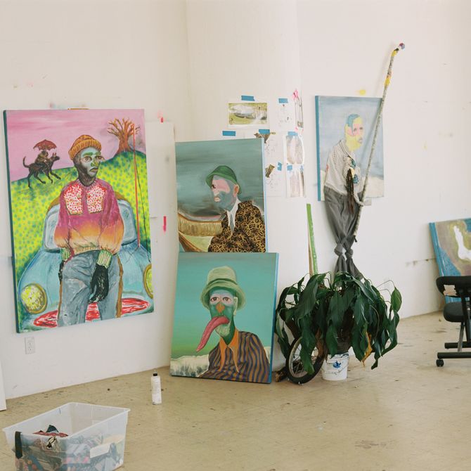 shot of the artist's studio with images taped to the wall and numerous canvases hung up or resting on the floor depicting surrealist portraits