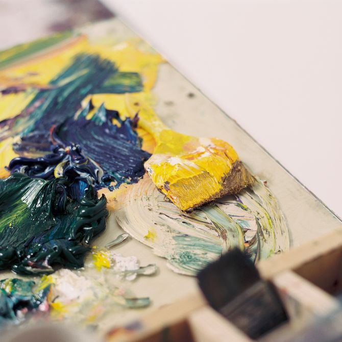 Close-up photo of oil paints in yellow and dark green and blue layered heavily onto a mixing palette