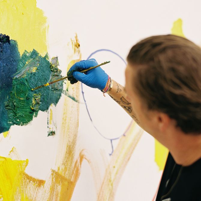 Friedrich Kunath focusing on a canvas with mixed green paint which he is working into with a small paintbrush
