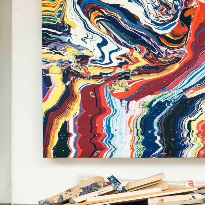 large colourful painting hung on a white wall with blocks of wood underneath
