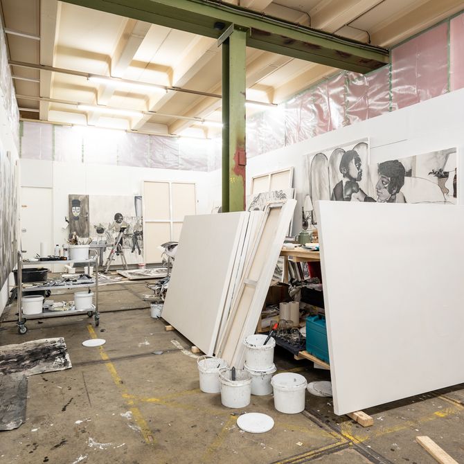 view of artist's studio with large empty canvases in the centre, numerous white paint pots and large paintings hung on the walls