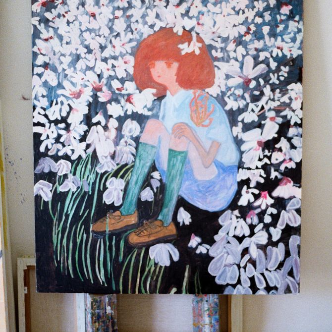 large painting of a girl sat in a flowery meadow propped up in a studio