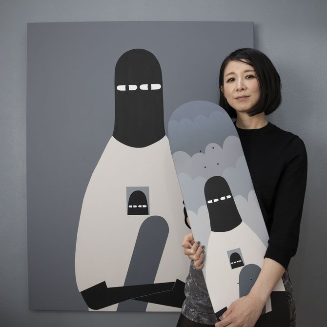 LY holding up a skateboard with her signature character LUV on it, in front of a painting of the same character