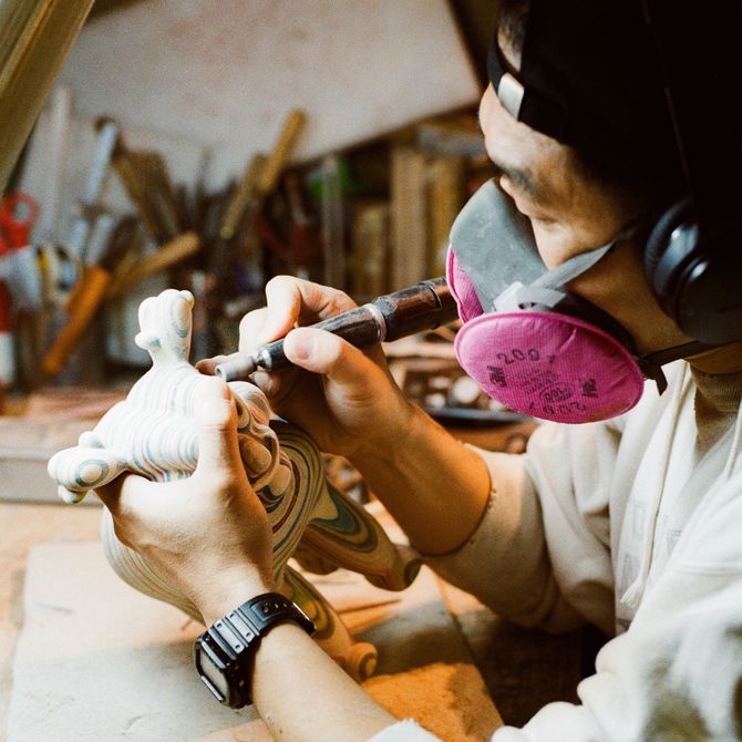 Close-up of Haroshi wearing a mask holding a sculpture he's working on