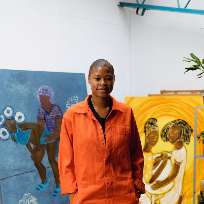 Sola Olulode stood in her studio surrounded by her paintings with her hands in her pockets