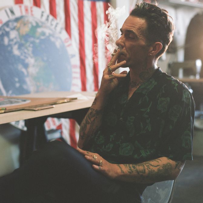 Cali Thornhill Dewitt sits at his desk smoking a cigarette in his studio