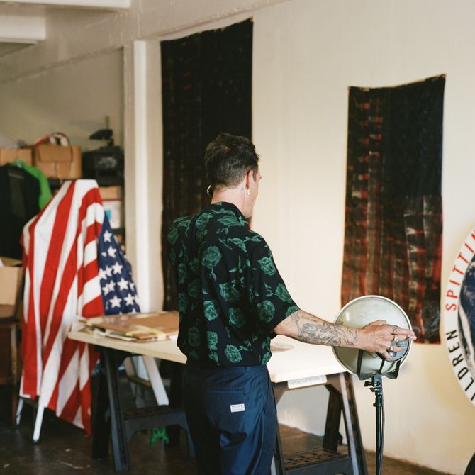 artist in his studio turning a lamp shade placed next to a table