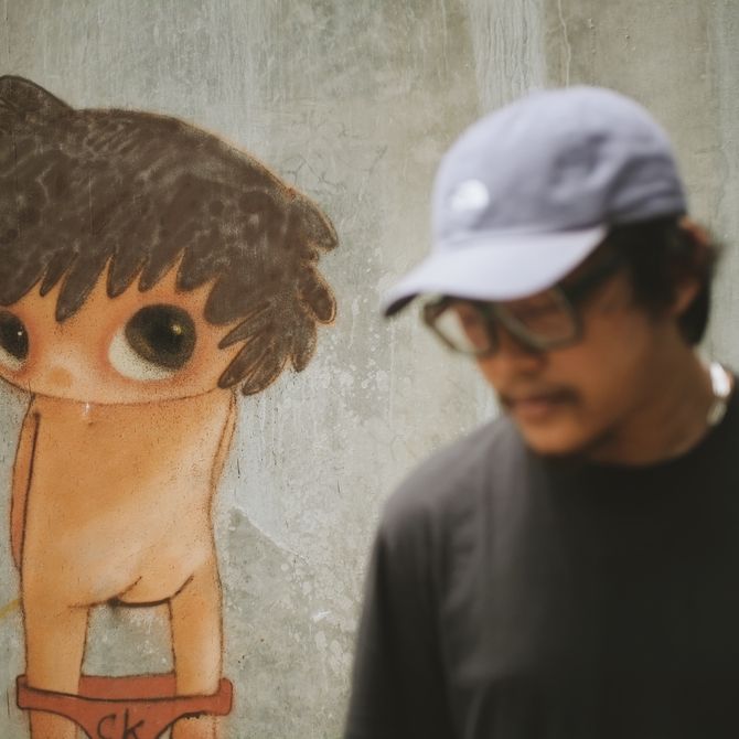 artist Ryol wearing a cap standing before a graffiti piece