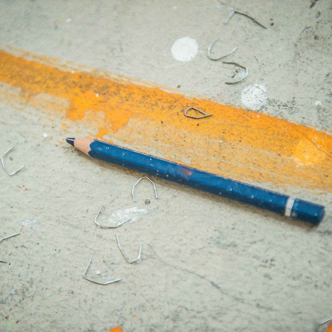 A blue pencil placed next to an orange line with staples around it