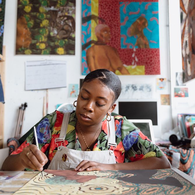 Shannon Bono concentrating on a painting on a table in front of her in her studio