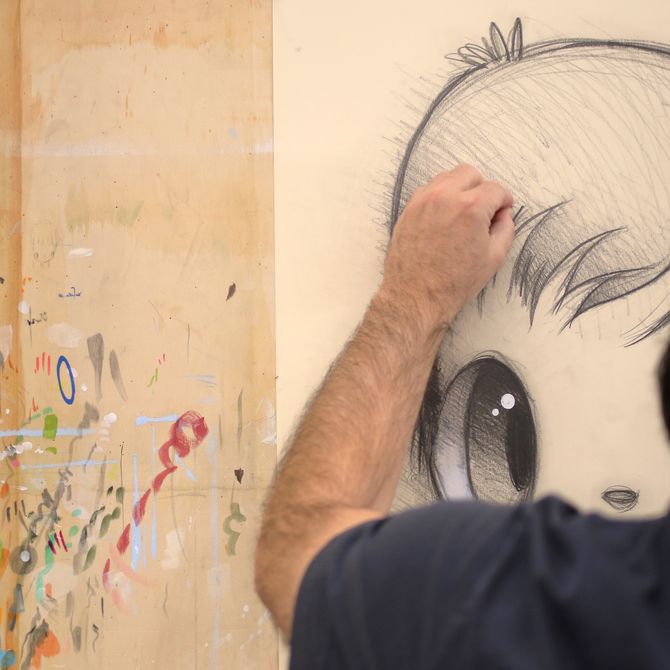 close-up of artist's hand working into a drawing on a wooden board in front of him