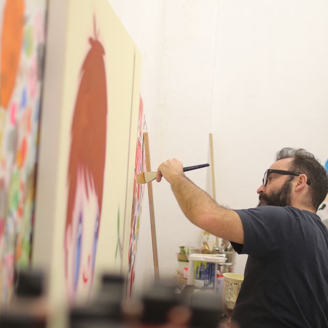 artist holding a paintbrush up to a row of canvases in his studio