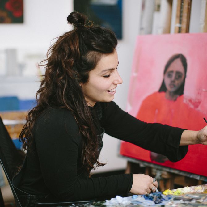 Aubrey Levinthal dipping a paint brush into oil paints in her studio