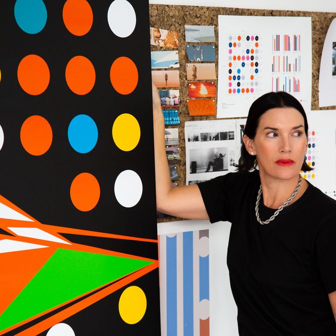 Sarah Morris standing next to her painting, in front of a pin board