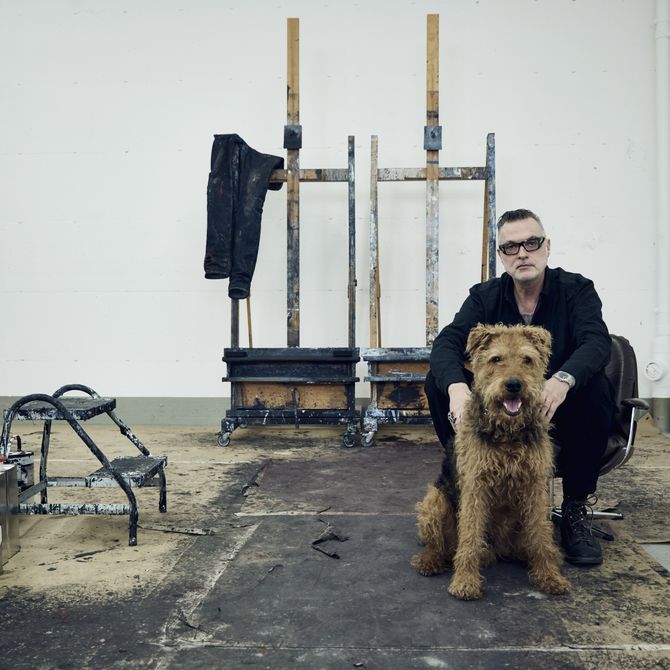 Artist sat behind his dog in his studio with two easels behind him