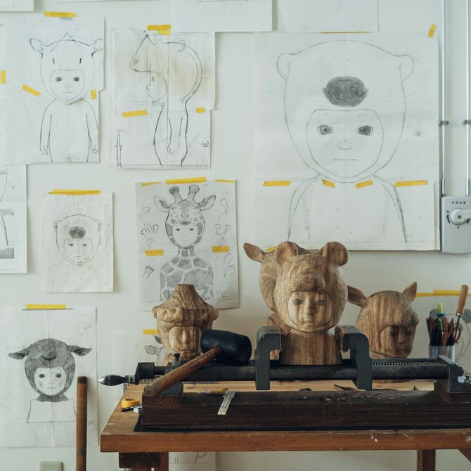 a wooden table with a selection of wooden sculptures on and an array of sketches of white pieces of paper taped to the wall behind