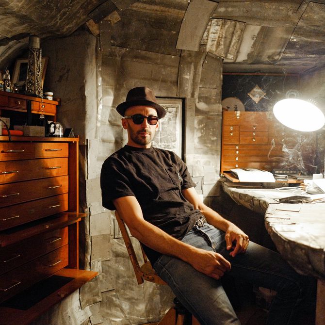 JR sitting in his studio at a work desk, in front of wooden drawers