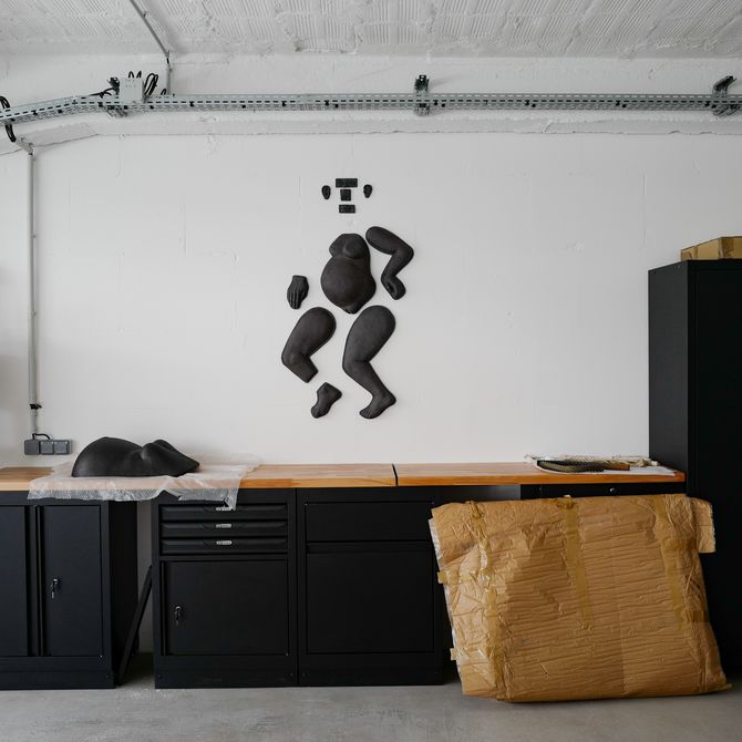 A black fragmented model of a pregnant body hangs on a white wall above a black work station