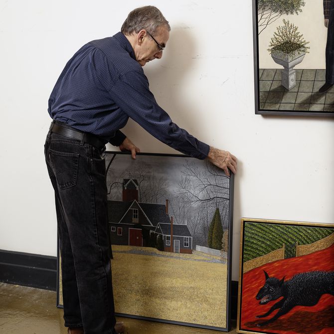 artist viewed from the side placing both hands onto a square painting that sits alongside two other paintings