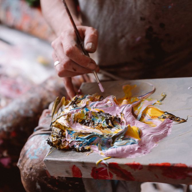 A paintbrush being dipped into paint with pink and yellow tones