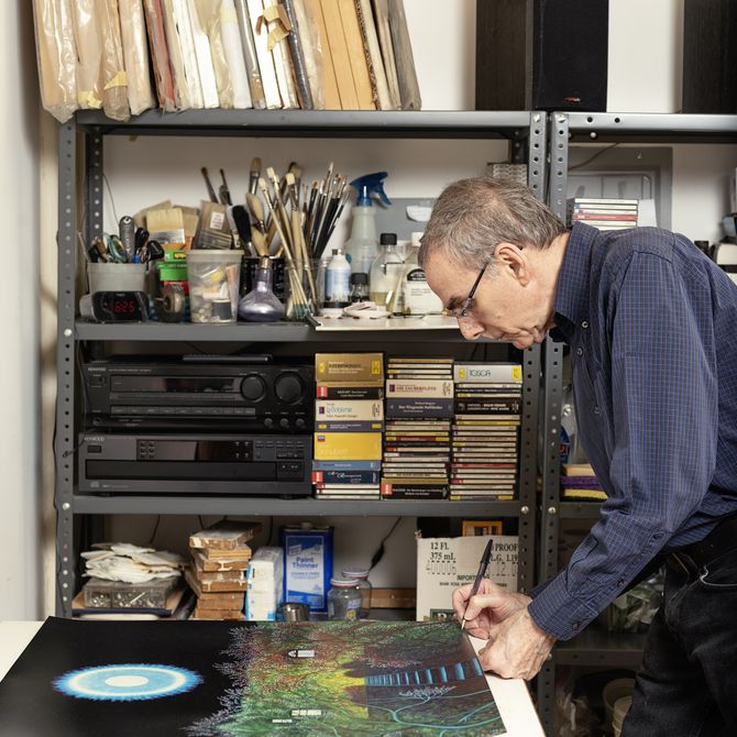 artist leaning over his desk space in his studio signing the bottom corner of a painting
