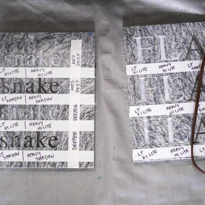 two grey works of art with repeated words engraved into them and white tape creating various lines across them