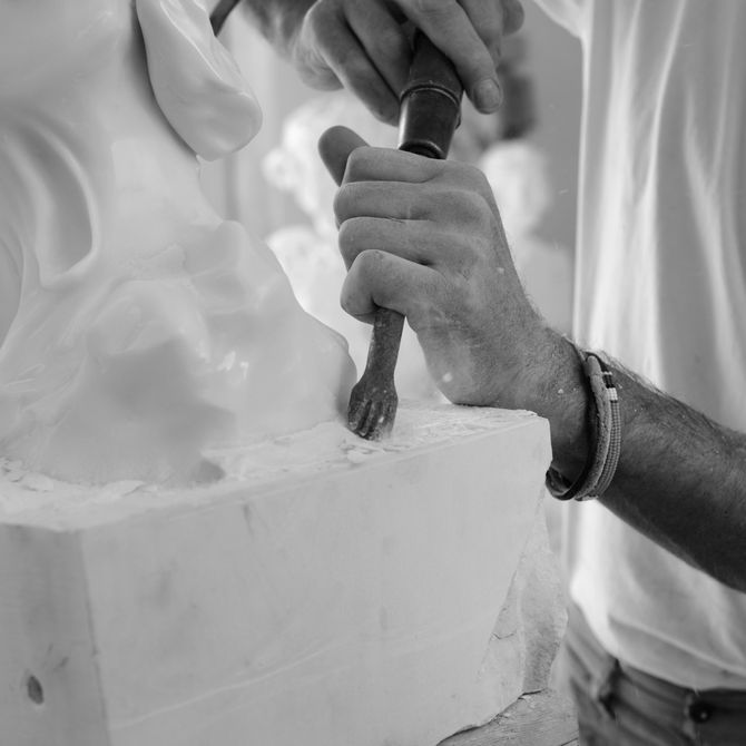 close-up of artist using a tool to chip away and carve out a marble sculpture from the block