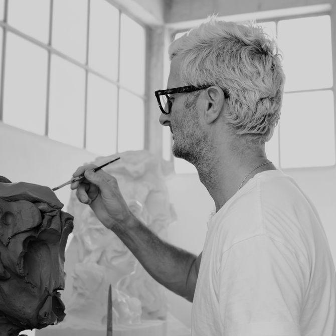 side view of Kevin Francis Gray working on a sculptural bust in front of him with a paintbrush