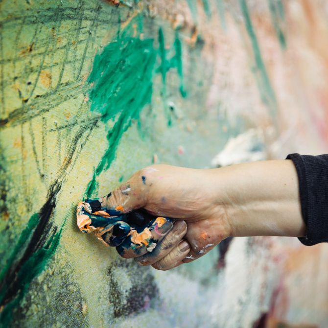 close-up of artist's hand covered in paint as he layers colours onto a canvas