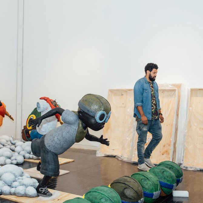 Hebru Brantley walking through large studio space surrounded by three large sculptures of his