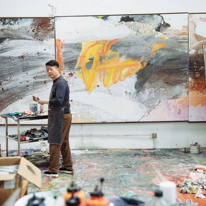 Wang Yan Cheng twisting to turn away from three large paintings on the wall in his studio