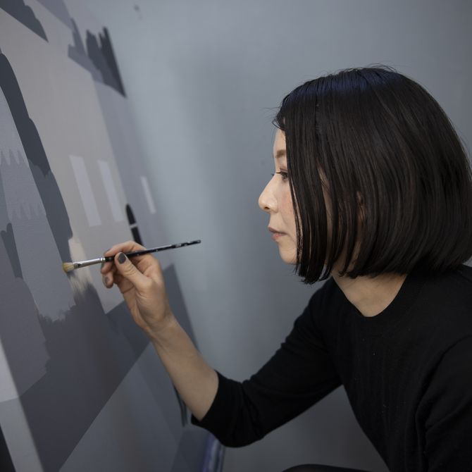 artist holding a paintbrush up to her canvas as she touches up some areas of grey