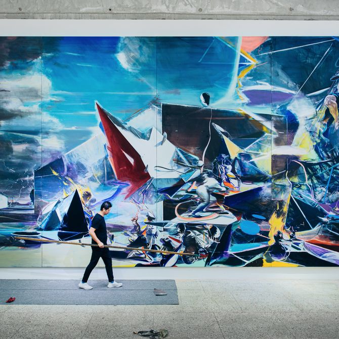 artist walking in front of huge wall mural painting holding a very long tool