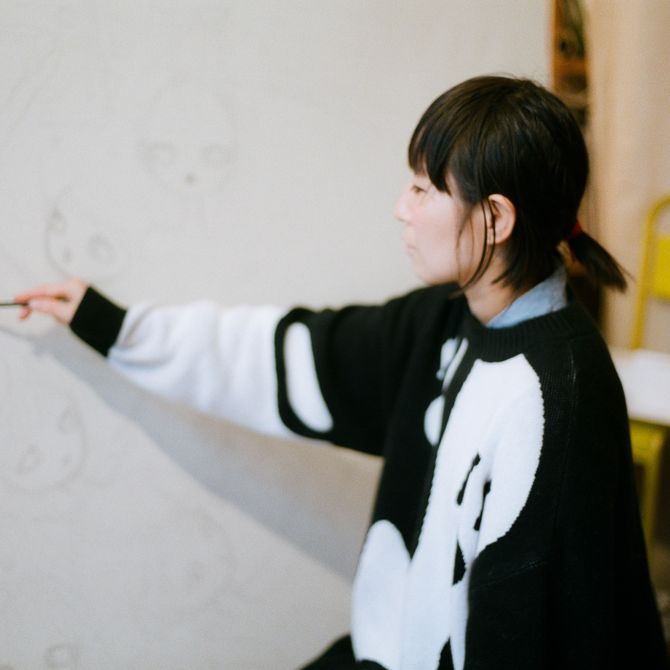 Aya Takano reaching forwards to raise a pencil to a canvas