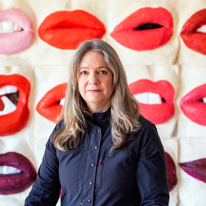 Gina Beavers smiling in front of a painting of lips
