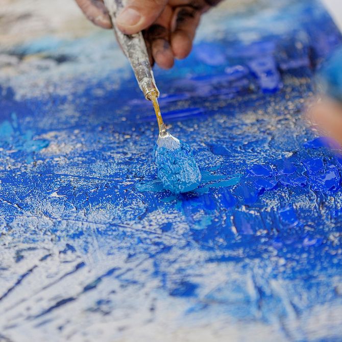 very close up photo of Jose Parla's hand applying blue paint to canvas with a palette knife