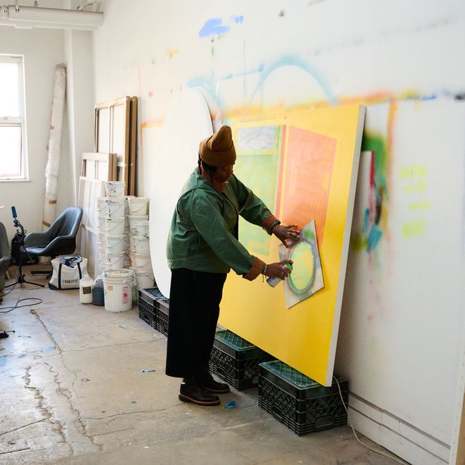 Nina Chanel spraying a yellow canvas leaned against studio wall