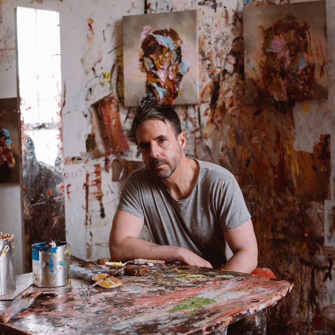 Antony sitting down in his studio surrounded by paintings and paint on the walls