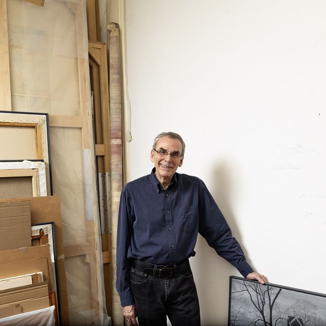 Scott Kahn smiling with one hand placed leaning against a painting of his