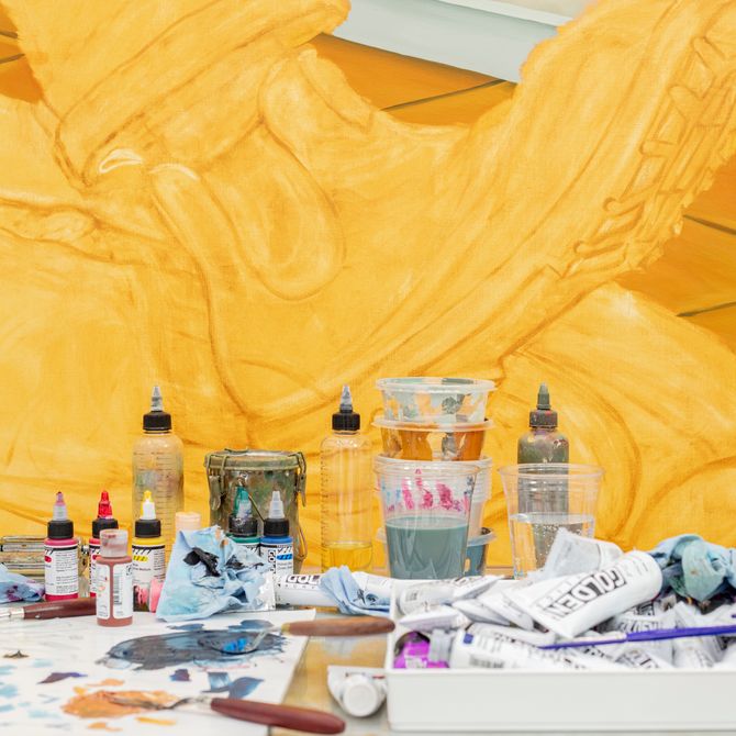 various tubes and pots of paints in front of a yellow painting