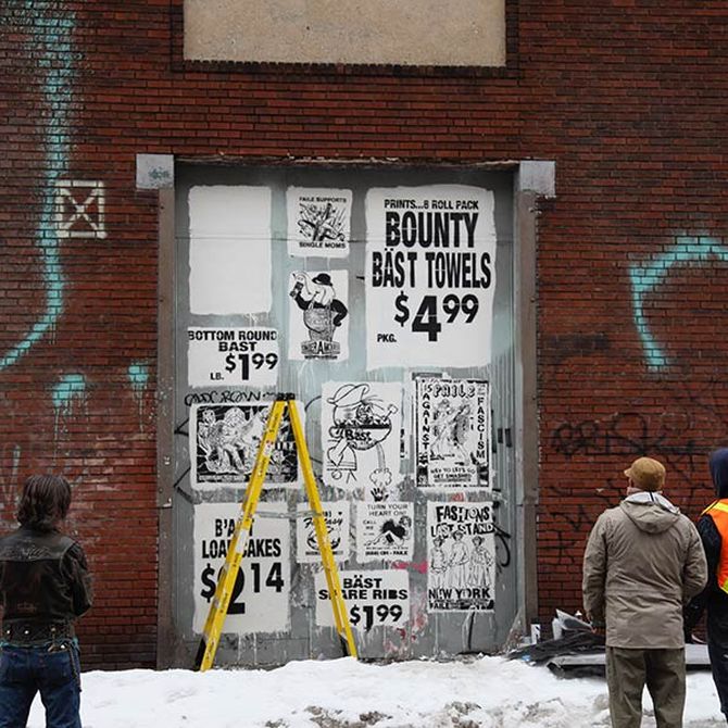 3 people looking at a series of faux advertisements on a large industrial door