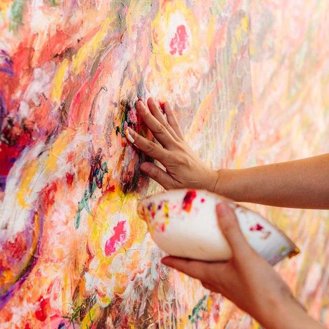A hand adding paint to the surface of a colourful abstract painting