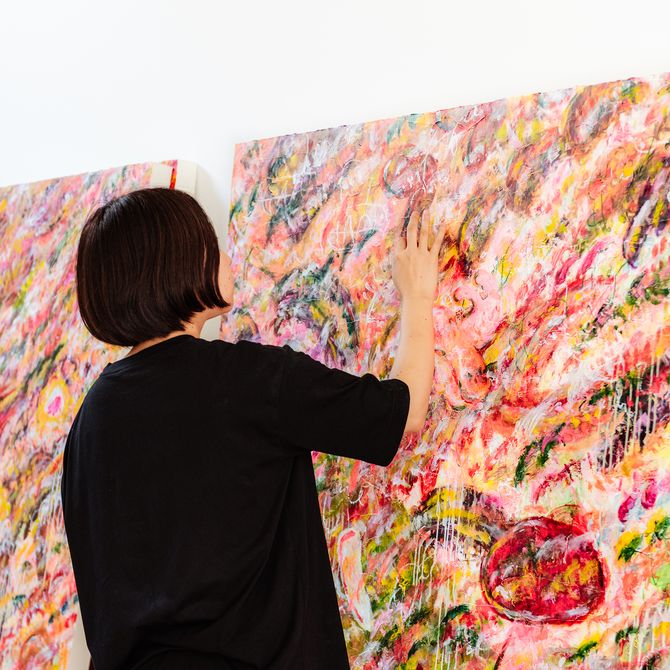 Ayako Rokkaku wearing a black T-shirt, touching the surface of a large painting
