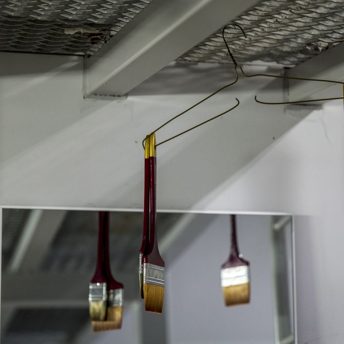 Paintbrushes hanging from coat hanger on studio ceiling