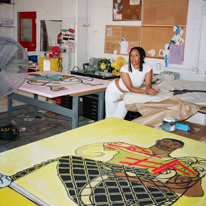 Tschabalala Self leaning on a table in her studio, a large yellow painting is visible in the foreground